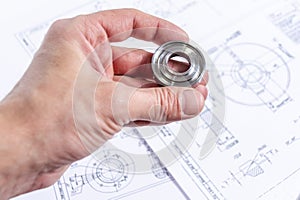 Engineers hand holds a metal part against the background of technical drawings. Quality control of parts machined on a lathe