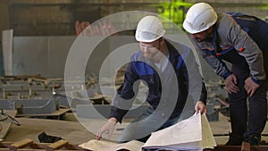 Engineers look at building plans and discuss stages of construction in heavy industry factory