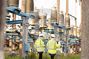 Engineers men in warm clothes use digital tablet computer discuss work walking against power electric substation