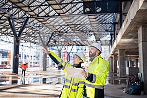 Engineers standing outdoors on construction site, holding tablet.
