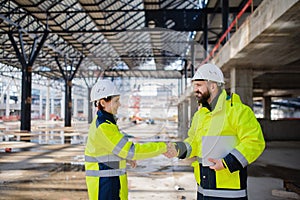 Engineers with tablet standing on construction site, shaking hands.