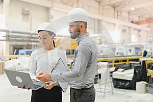 Engineers using laptop and discussing project in factory