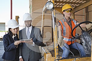 Engineers using tablet PC with female industrial worker driving forklift truck