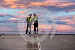 Engineers walking on roof inspect and check solar cell panel by hold equipment box and radio communication ,solar cell is smart gr