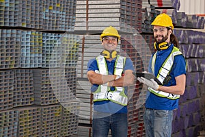 Engineers with yellow hardhat inspect steel bars with tablet in a factory