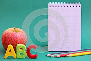 English ABC alphabet letters next to apple. Colored pencils and an empty Notepad page