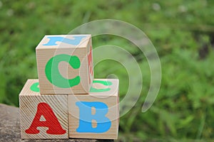 English ABC letters on wooden toy blocks outdoors on a green grass background