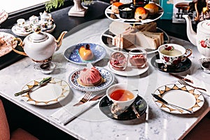 English afternoon tea set including hot tea, pastry, scones, sandwiches and mini pies on marble top table