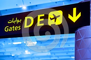 English and Arabian yellow illuminated sign at airport with gate letters D and E