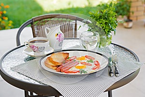 English breakfast on summer terrace: fried eggs, sausage, tomatoes, and toasts.