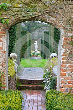 English garden gate with a marmoreal sculpture between shrubs of box trees