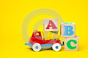 English letters ABC on wooden blocks in a toy plastic truck on a yellow background