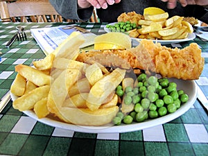 English meal of battered fish chips and peas on a plate.