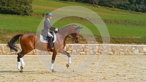 English rider on horseback riding trot around the sandy arena in the countryside