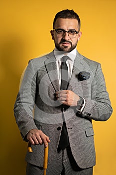 English style handsome young man wearing grey suit with one hand lifted standing with cane or umbrella in his hand