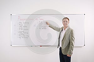 English teacher giving lesson on prepositions of time near whiteboard in classroom