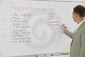 English teacher giving lesson on prepositions of time near whiteboard in classroom