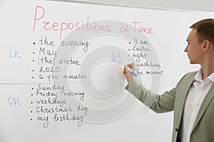 English teacher giving lesson on prepositions of time near whiteboard in classroom