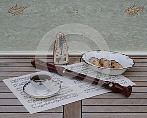 English teacup with saucer and a cake bowl with cookies metronome for music and a block flute on a sheet of music