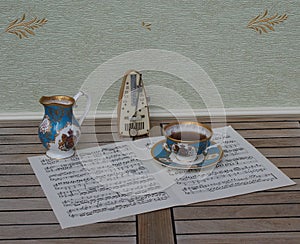 English teacup with saucer, cream jug, fine bone china porcelain, and a metronome for music on a sheet of music