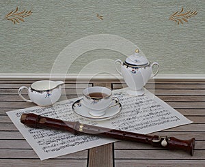 English teacup with saucer, cream jug and sugar bowl, fine bone china porcelain, and a block flute on a sheet of music