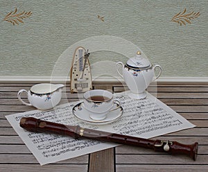 English teacup with saucer, cream jug and sugar bowl, metronome for music and a block flute on a sheet of music