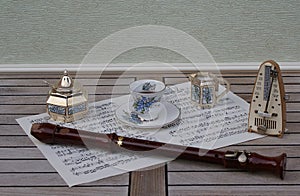English teacup and saucer, cream jug, sugar bowl, sugar spoon and metronome for music and a block flute on a sheet of music