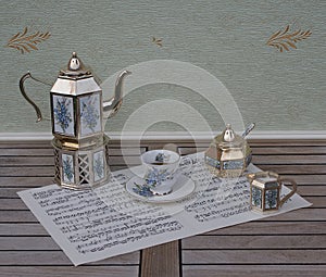 English teacup, saucer, silver-plated teapot on a silver stove, cream jug, sugar bowl and sugar spoon, on a sheet of music