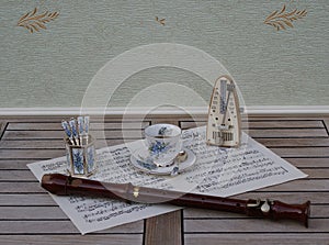 English teacup and saucer spoon vase, teaspoon, with floral decor, and metronome for music and a block flute on a sheet of music