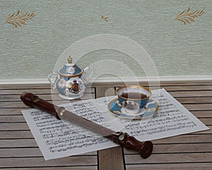 English teacup with saucer, sugar bowl, fine bone china porcelain, and a block flute on a sheet of music