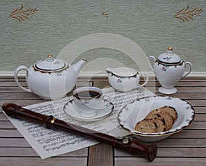 English teacup with saucer, teapot, cream jug, sugar bowl, a cake bowl and a block flute on a sheet of music