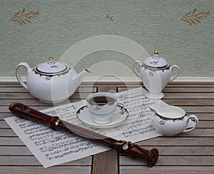 English teacup with saucer, teapot, cream jug and sugar bowl, fine bone china porcelain, and a block flute on a sheet of music