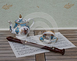 English teacup with saucer and teapot, fine bone china porcelain, and a block flute on a sheet of music