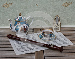 English teacup with saucer and teapot, fine bone china porcelain, metronome for music and a block flute on a sheet of music