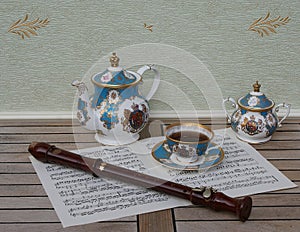 English teacup with saucer, teapot, and sugar bowl and a block flute on a sheet of music