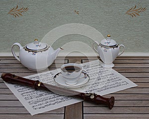 English teacup with saucer, teapot and sugar bowl, fine bone china porcelain, and a block flute on a sheet of music