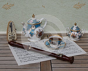 English teacup with saucer, teapot and sugar bowl, metronome for music and a block flute on a sheet of music