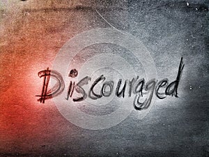 the English word discouraged written by pencil on the grey and orange wall background texture photo