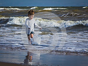 Engrossed enthusiastic boy running in the ebullient waves. Impression, experience, summer fun moments, delight