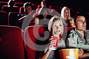 Engrossed in a great movie. A beautiful woman drinking a refreshment and eating popcorn with her boyfriend at the movies