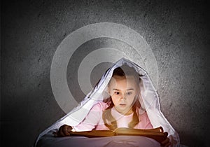 Engrossed little girl reading book in bed