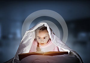 Engrossed little girl reading book in bed