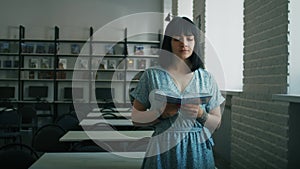 Engrossed woman reading book standing in a library. Informative portrait with depth of field. Continuous learning and