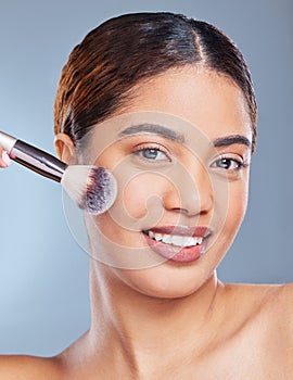 Enhance the beauty you already possess. a young woman applying makeup to her face against a grey background.