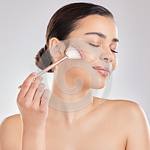 Enhancing my natural beauty. a young woman applying makeup to her face against a grey background.