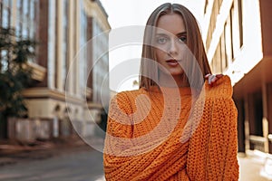 Enigmatic young woman in orange braided sweater with long sleeves