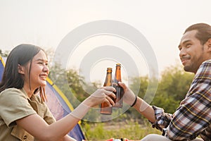 Enjoy asian young woman, girl and man cheering with beer bottle, sitting on chair . Adventure couple, people camping in forest.