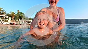 Enjoy a fun family holiday by the beach as a toddler boy, filled with laughter and joy, learns to swim with his mother