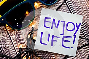 Enjoy life motivational handwritten message on a paper with blue color on wooden background with lights spread in unmistakable hea