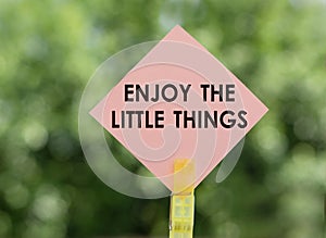 Enjoy the little things - text on pink note paper on green background. Concept for confidence, courage and motivation. Sign of